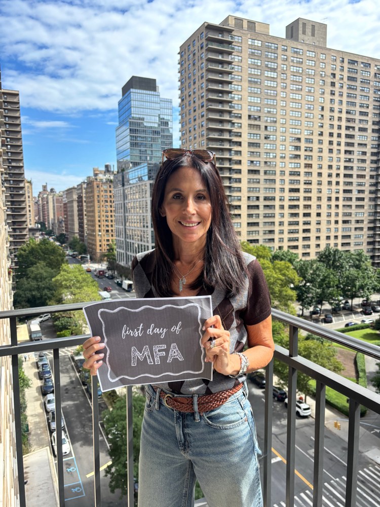 Erica Lyons holding a first day of MFA sign on a New York City balcony
